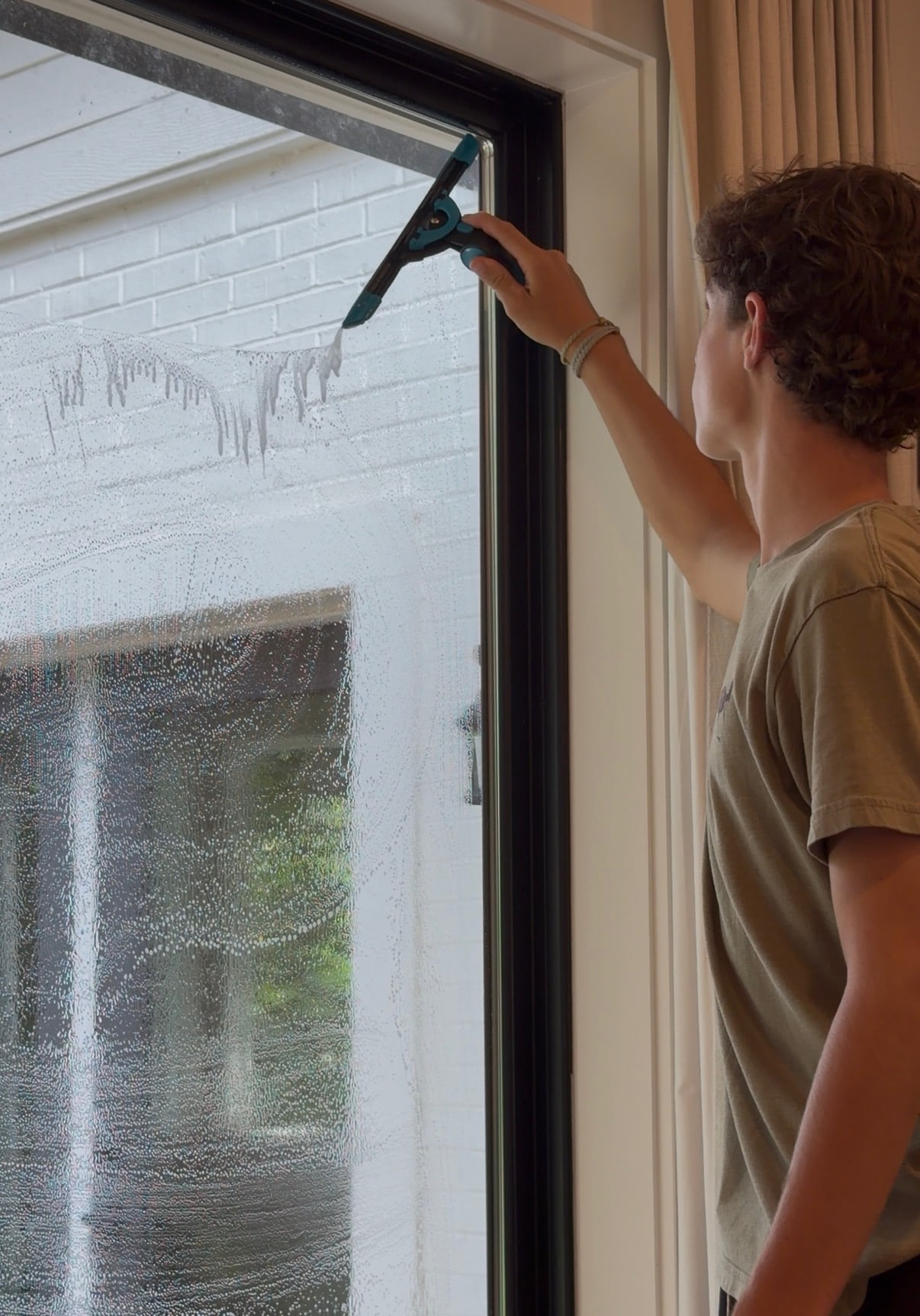 Brooks Safley cleaning an interior window by hand with a squeegee.