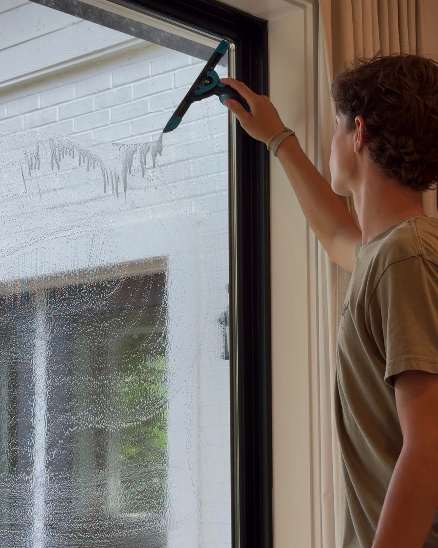 Brooks Safley hand-cleaning an interior window with a squeegee.
